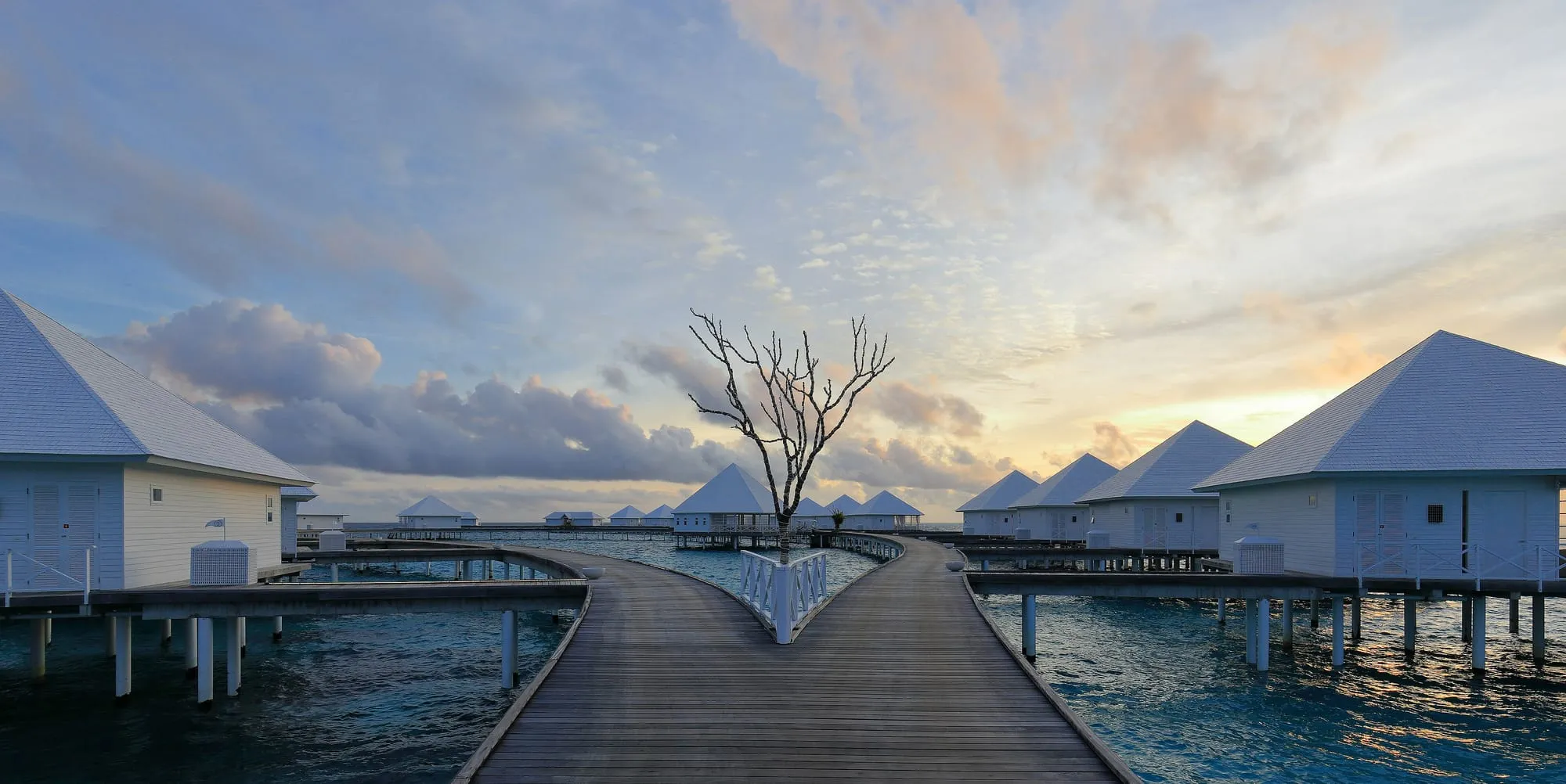 Passerella in legno verso le ville sull’acqua di un resort alle Maldive, al tramonto