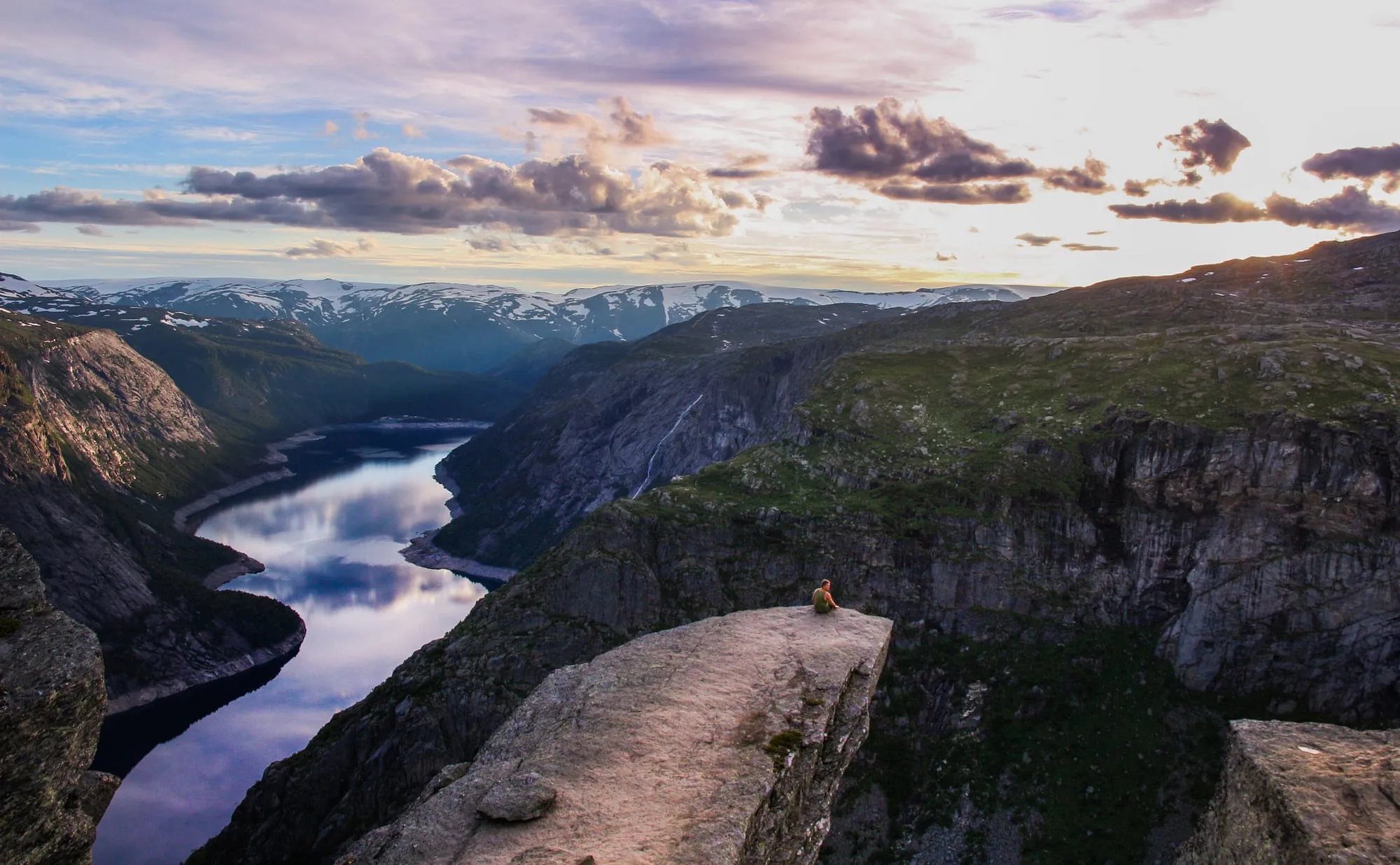 Viaggiatore da solo seduto sulla roccia di Trolltunga, in Norvegia, al tramonto sul fiordo