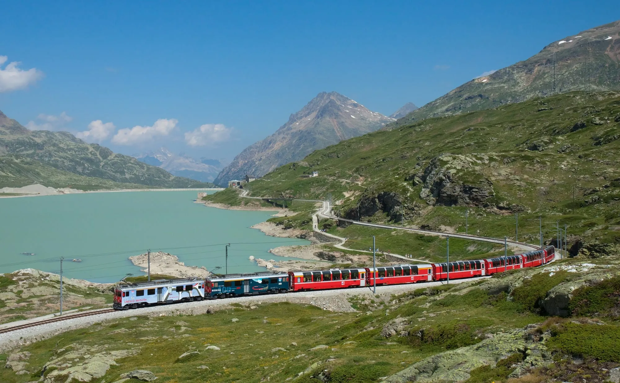 The red Bernina Express train running along Lago Bianco in the mountains